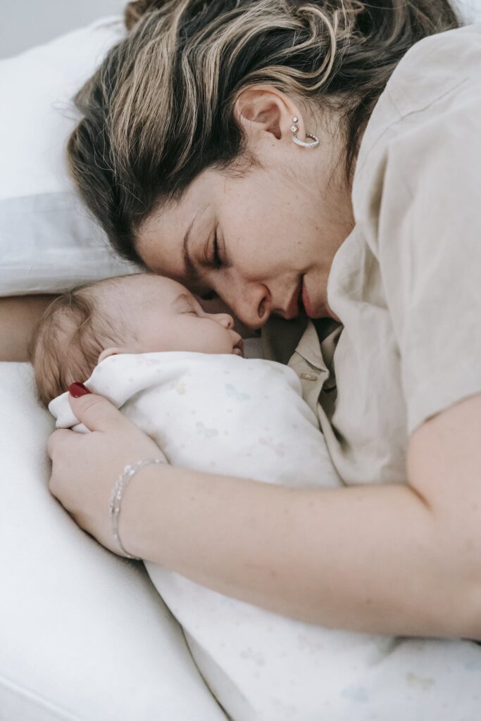 Mother with sleeping newborn baby on bed
